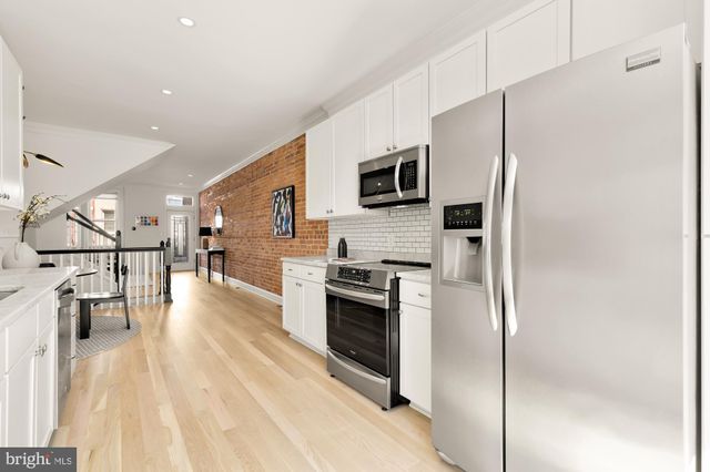 a kitchen with stainless steel appliances a refrigerator a stove top oven a sink dishwasher and white cabinets with wooden floor