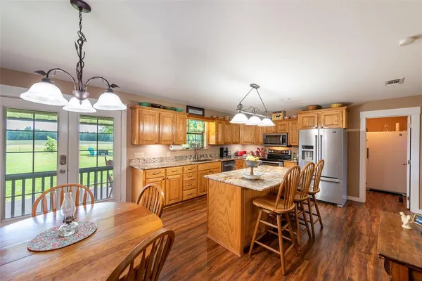 a kitchen with stainless steel appliances granite countertop a stove top oven a sink a dining table and chairs with wooden floor