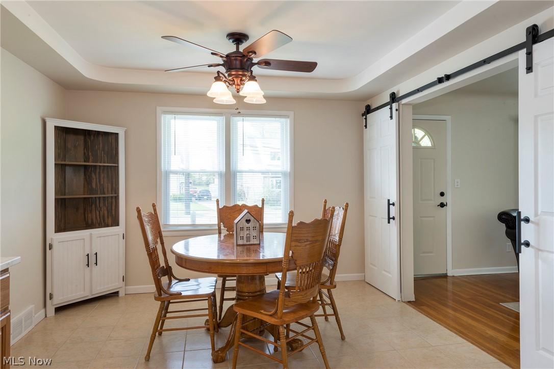 13175 McCracken Road Cleveland, OH 44125 - Photo 11 of 48 Eat-in kitchen dining area featuring ceiling fan, a tray ceiling, light wood-type flooring, and a barn door