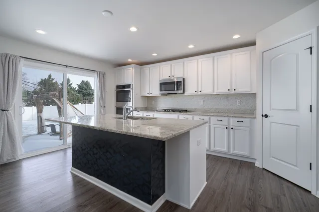 a kitchen with kitchen island granite countertop a stove a sink and white cabinets with wooden floor