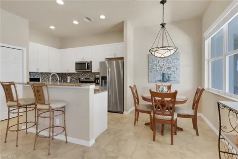 a kitchen with stainless steel appliances granite countertop a dining table chairs refrigerator and microwave