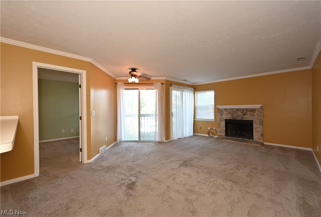 28140 Detroit Road, Unit A1 Westlake, OH 44145 - Photo 3 of 30 Unfurnished living room featuring a stone fireplace, ceiling fan, a textured ceiling, crown molding, and carpet flooring