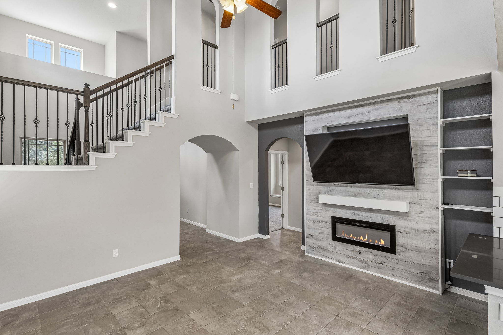 689 Nautical Loop Kyle, TX 78640 - Photo 9 of 34 A well-lit living area boasts high ceilings, elegant staircase, and a modern fireplace feature wall with built-in shelving.