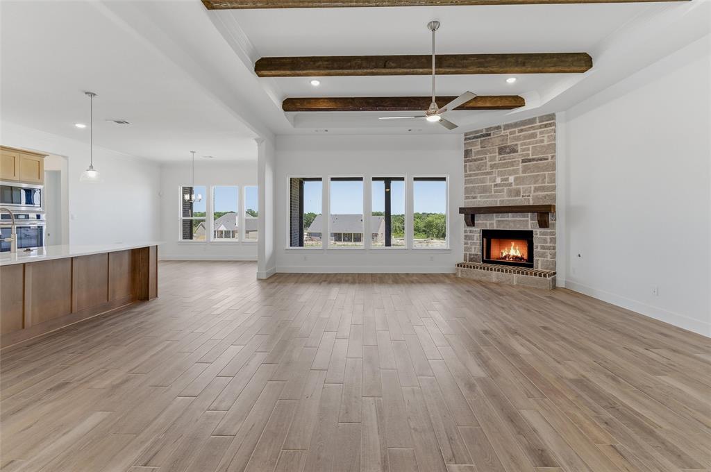 815 Vly Rdg Road Van Alstyne, TX 75495 - Photo 11 of 29 Spacious living area featuring wood-finish flooring, a stone fireplace with a wood mantle, ceiling beams, and a ceiling fan