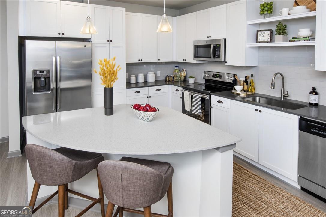 6919 Peachtree Road, Unit 545 Atlanta, GA 30328 - Photo 3 of 38 Kitchen featuring backsplash, stainless steel appliances, sink, hanging light fixtures, and light hardwood / wood-style flooring