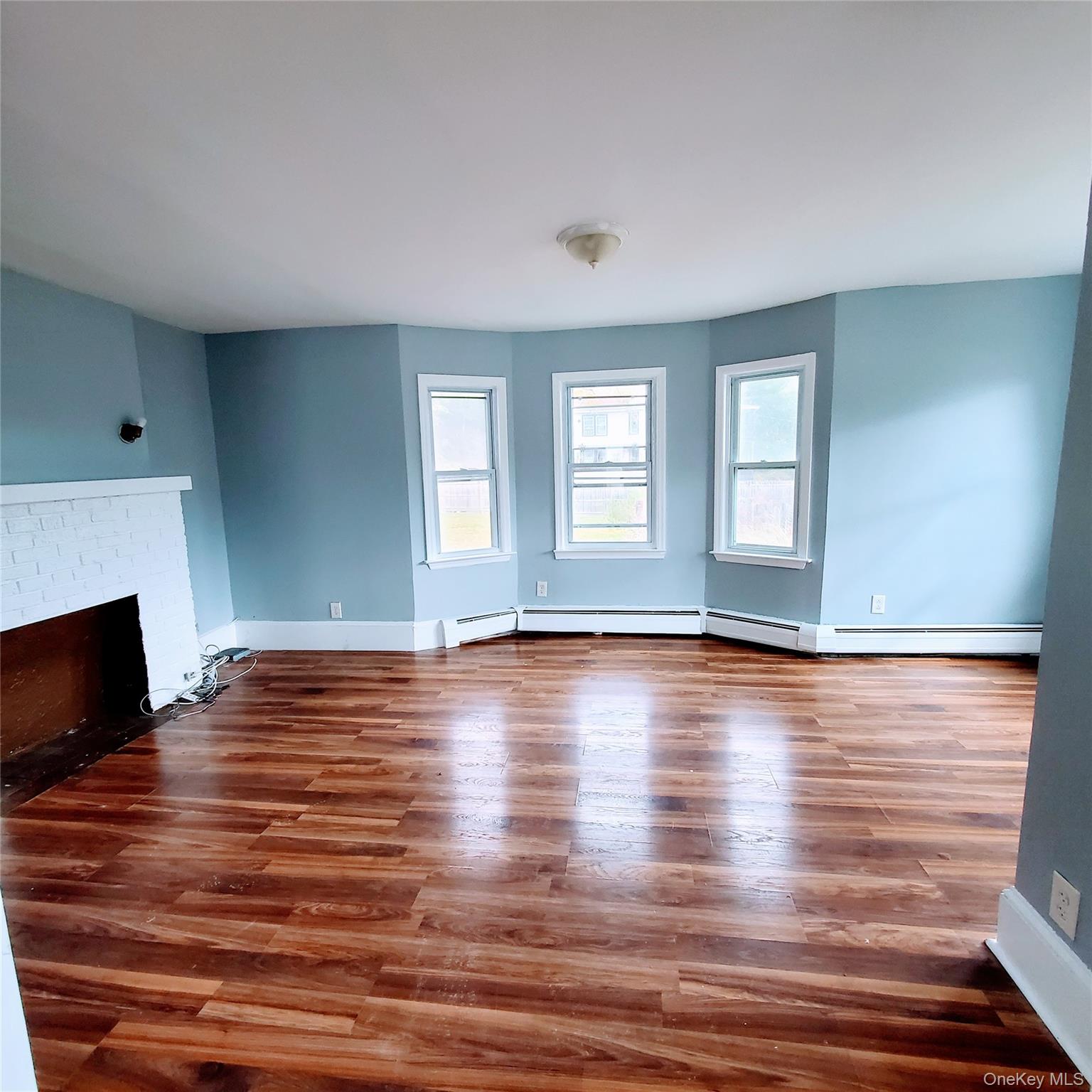 210 Smith Street Poughkeepsie, NY 12601 - Photo 7 of 44 Unfurnished living room featuring wood finished floors, a brick fireplace, and a baseboard radiator