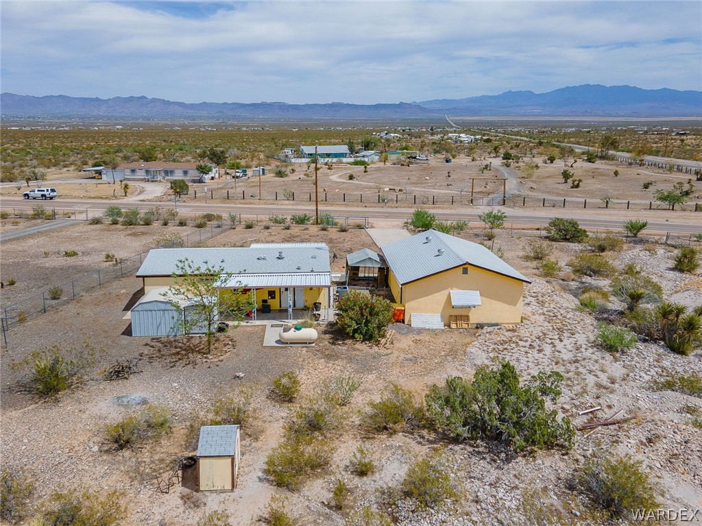 2465 Egar Road Golden Valley, AZ 86413 - Photo 81 of 98 The property features two structures with yellow exteriors and light-colored roofs, set within a landscape of arid vegetation and distant mountains