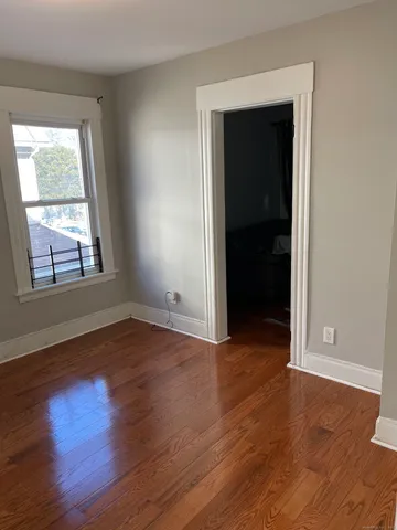 a view of an empty room with wooden floor & window