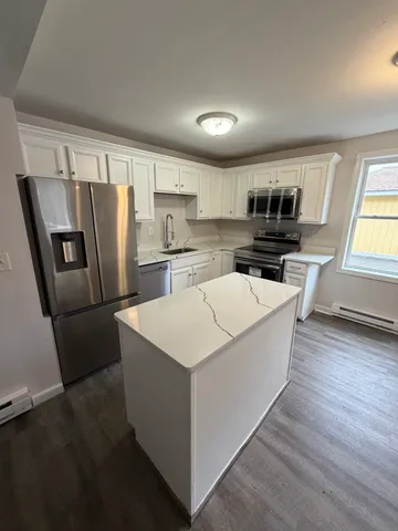 a living room with stainless steel appliances a refrigerator a sink a stove a microwave a center island and a window