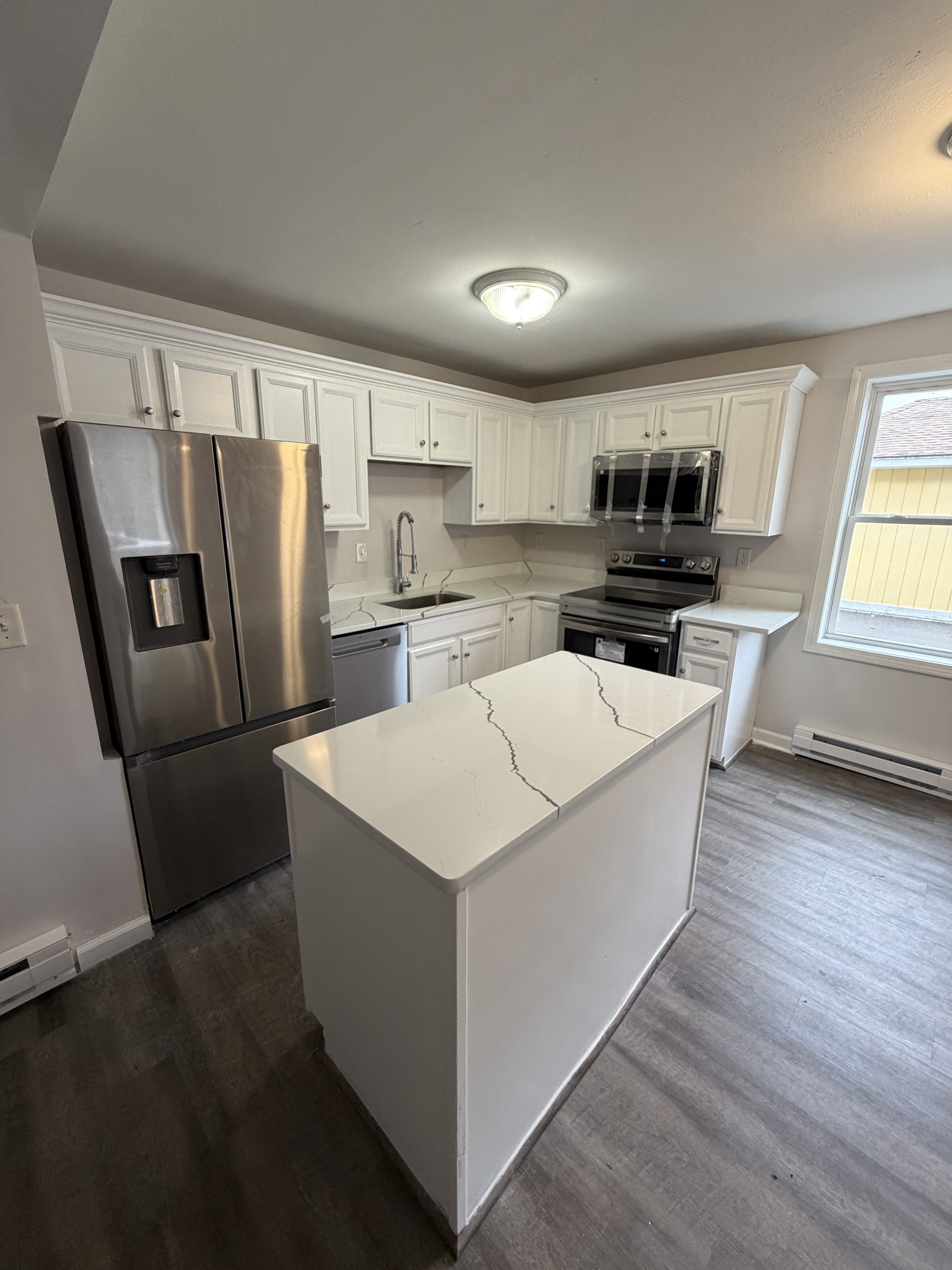 a living room with stainless steel appliances a refrigerator a sink a stove a microwave a center island and a window