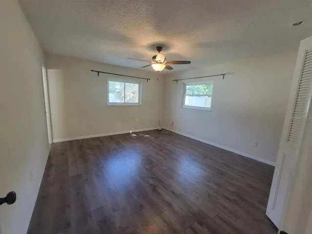 an empty room with wooden floor ceiling fan and windows