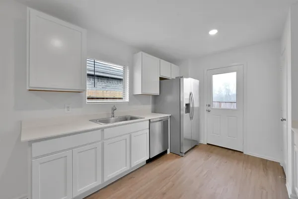 a kitchen with a sink dishwasher a refrigerator and white cabinets with wooden floor