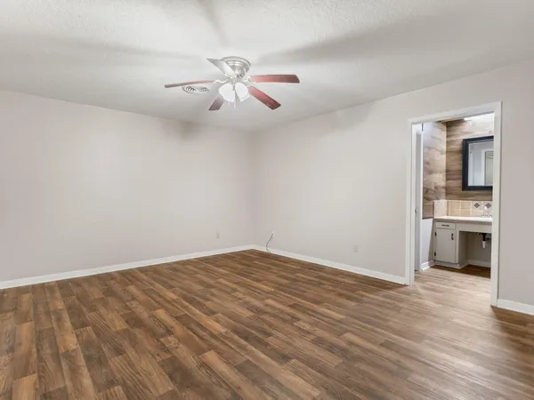 an empty room with wooden floor chandelier fan and kitchen view