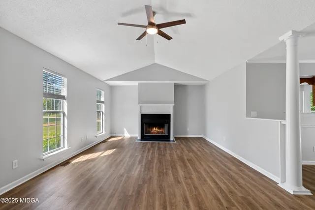 an empty room with windows a fireplace a ceiling fan and wooden floor