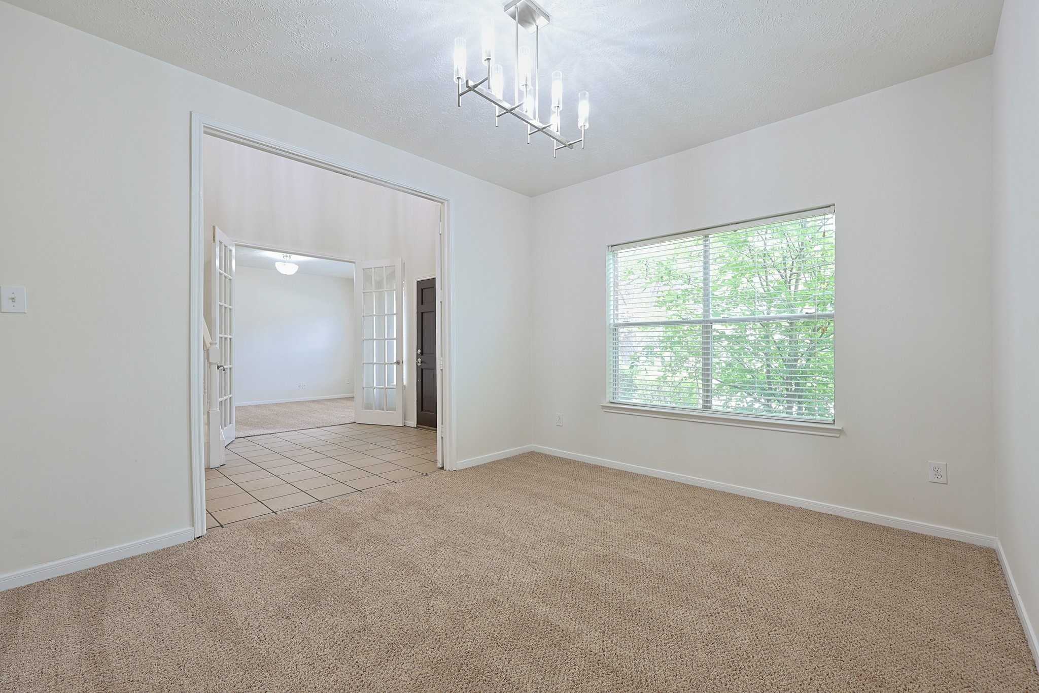 23019 Eastgate Village Drive Spring, TX 77373 - Photo 19 of 46 Bright room with neutral carpet, modern light fixture, and large window offering natural light. It opens to another space with tiled flooring and French doors, creating an inviting flow.