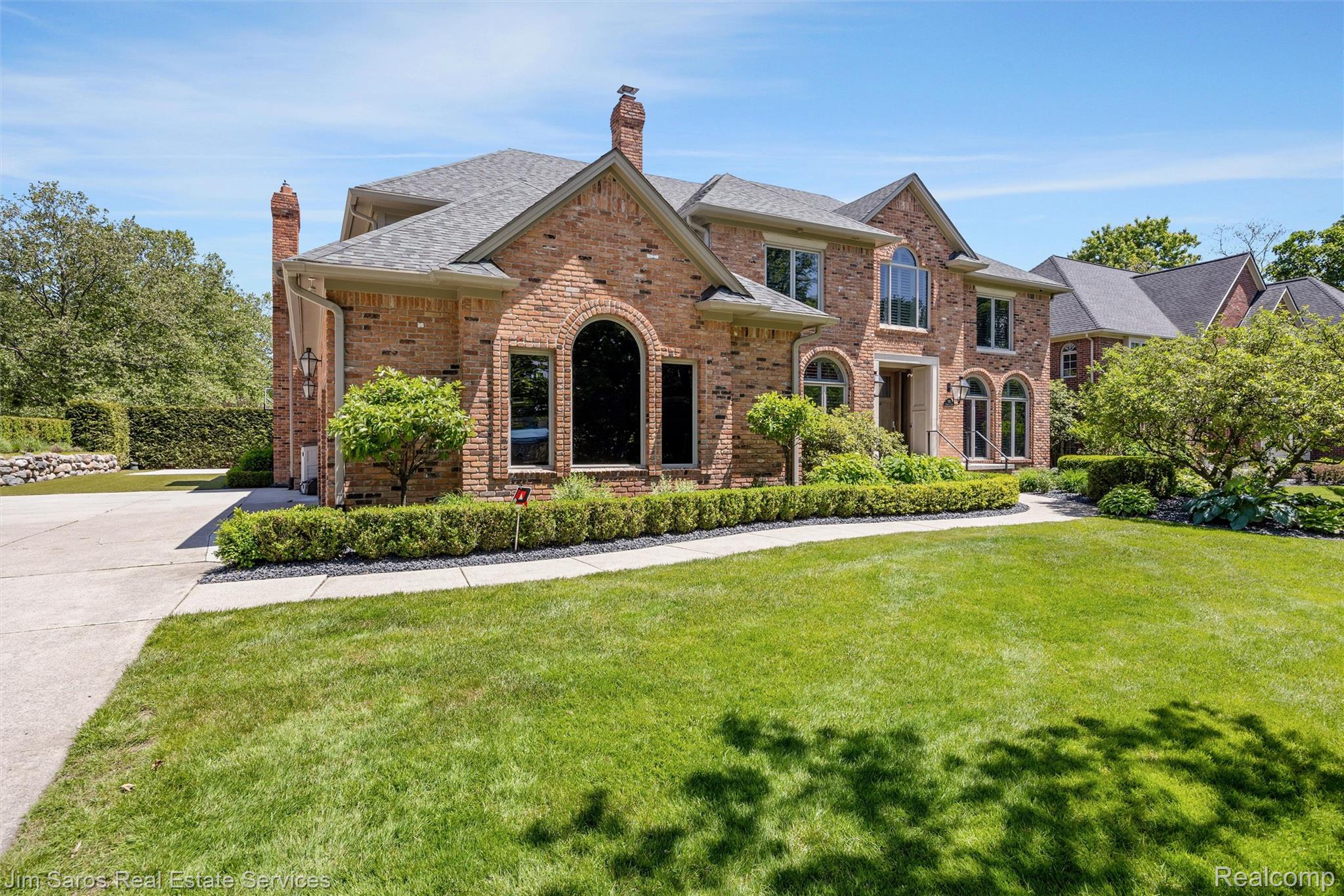 Brick exterior residence featuring a symmetrical facade, arched windows, a multi-gabled roofline, mature landscaping, and a concrete driveway