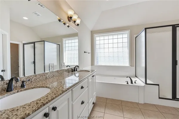 a bathroom with a granite countertop bathtub a double vanity sink a vanity a window and a mirror