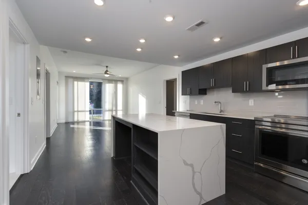 a kitchen with stainless steel appliances kitchen island granite countertop a stove top oven a sink dishwasher a refrigerator and white cabinets with wooden floor