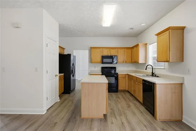 a large kitchen with stainless steel appliances a sink dishwasher a refrigerator a stove top oven a counter space and wooden floor