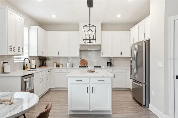 a kitchen with stainless steel appliances granite countertop a refrigerator a sink dishwasher a stove and white cabinets with wooden floor