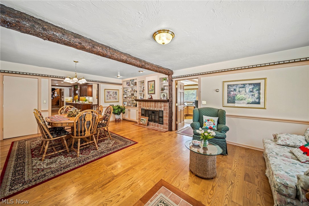 8801 Bunker Road Orwell, OH 44076 - Photo 24 of 50 Dining space featuring beam ceiling, light wood-style flooring, a chandelier, a textured ceiling, and a brick fireplace
