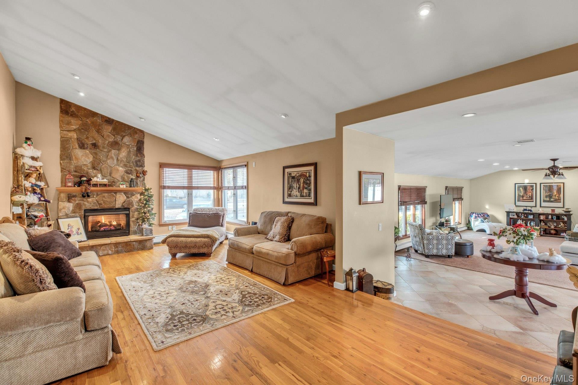1044 Commack Road Dix Hills, NY 11746 - Photo 10 of 29 Living room featuring lofted ceiling, a stone fireplace, light wood-type flooring, healthy amount of natural light, and a ceiling fan