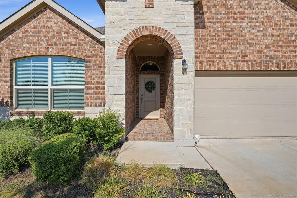 1812 Ruffian Road Granbury, TX 76049 - Photo 2 of 37 Brick and stone exterior with an arched entryway, featuring a prominent garage door and established landscaping
