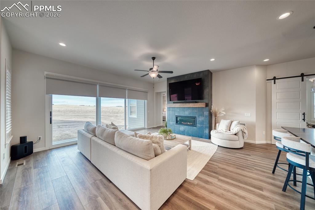 10059 Owl Perch Loop Colorado Springs, CO 80908 - Photo 22 of 50 Living area featuring a barn door, light wood-style flooring, a ceiling fan, a tile fireplace, and recessed lighting