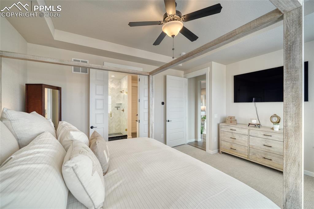 10059 Owl Perch Loop Colorado Springs, CO 80908 - Photo 37 of 50 Bedroom featuring a tray ceiling, light carpet, a ceiling fan, and ensuite bathroom
