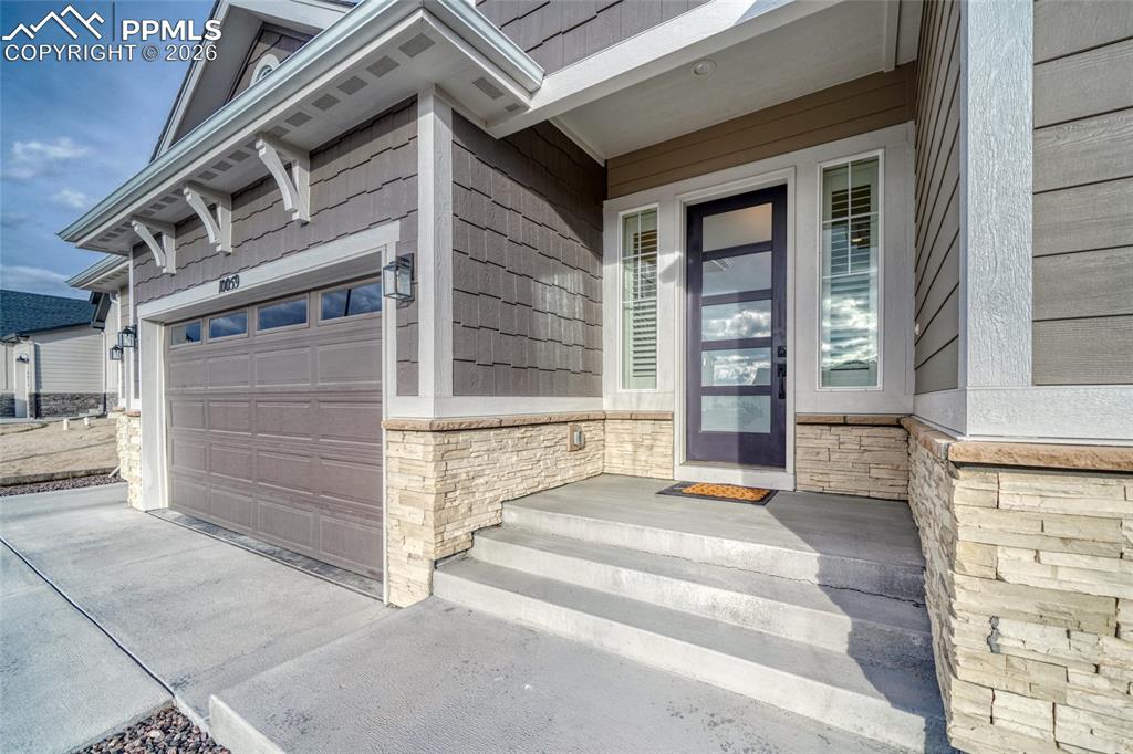 10059 Owl Perch Loop Colorado Springs, CO 80908 - Photo 8 of 50 View of exterior entry with stone siding, covered porch, driveway, and an attached garage