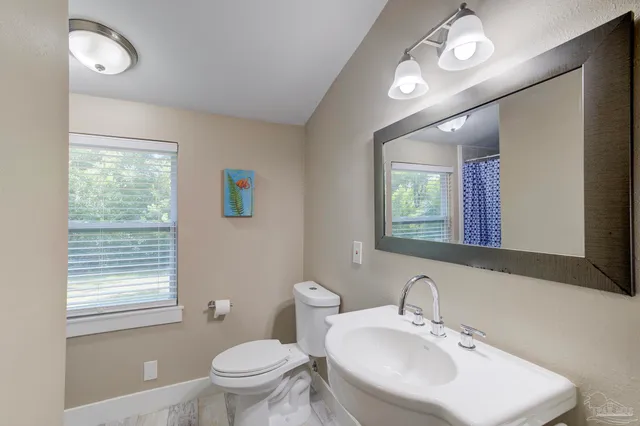 a bathroom with a toilet a sink a mirror and a window