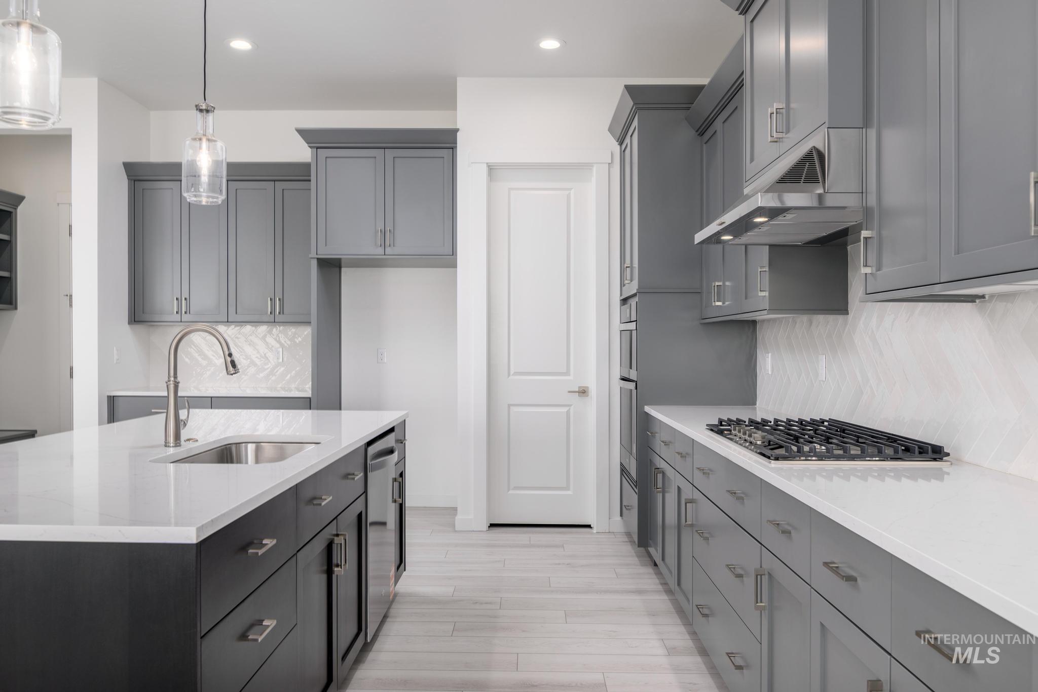 5416 Sparky Avenue Caldwell, ID 83607 - Photo 9 of 42 Kitchen featuring light stone counters, backsplash, hanging light fixtures, gray cabinetry, and recessed lighting