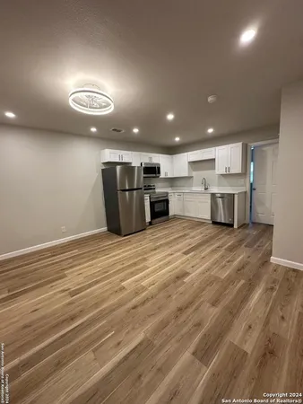 an empty room with wooden floor and kitchen view