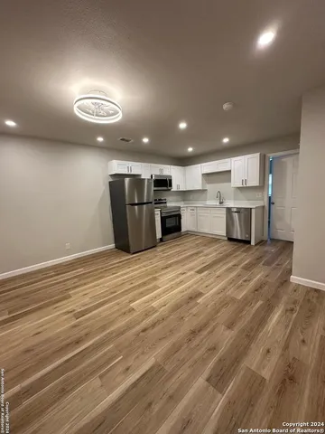 an empty room with wooden floor and kitchen view