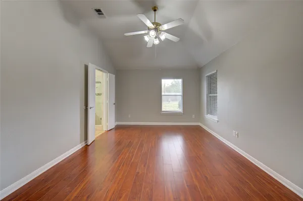 an empty room with wooden floor chandelier fan and windows