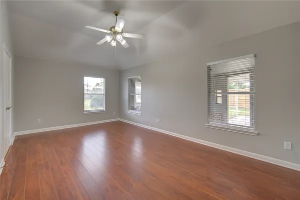 an empty room with wooden floor windows and fan