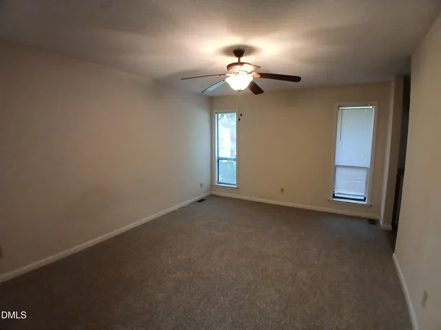 an empty room with a chandelier fan and windows