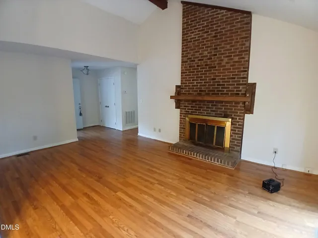 a view of an empty room with wooden floor and a fireplace