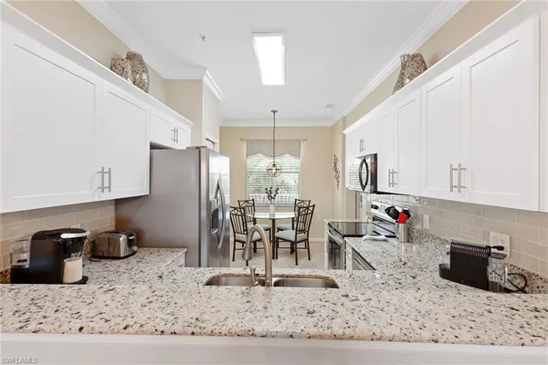 a kitchen with stainless steel appliances kitchen island granite countertop a dining table chairs and a refrigerator