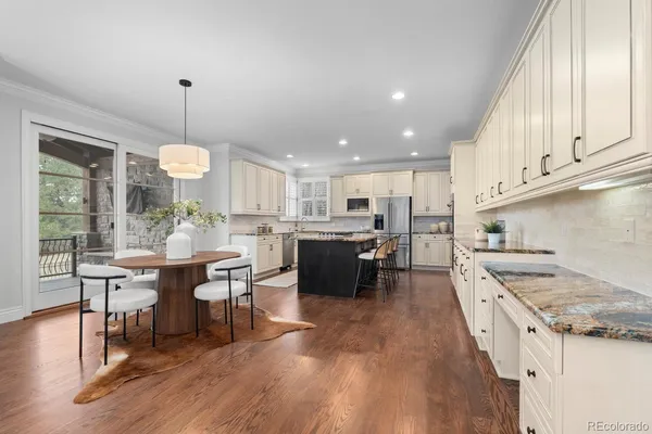 a open kitchen with stainless steel appliances granite countertop a stove top oven a refrigerator a dining table and chairs with wooden floor
