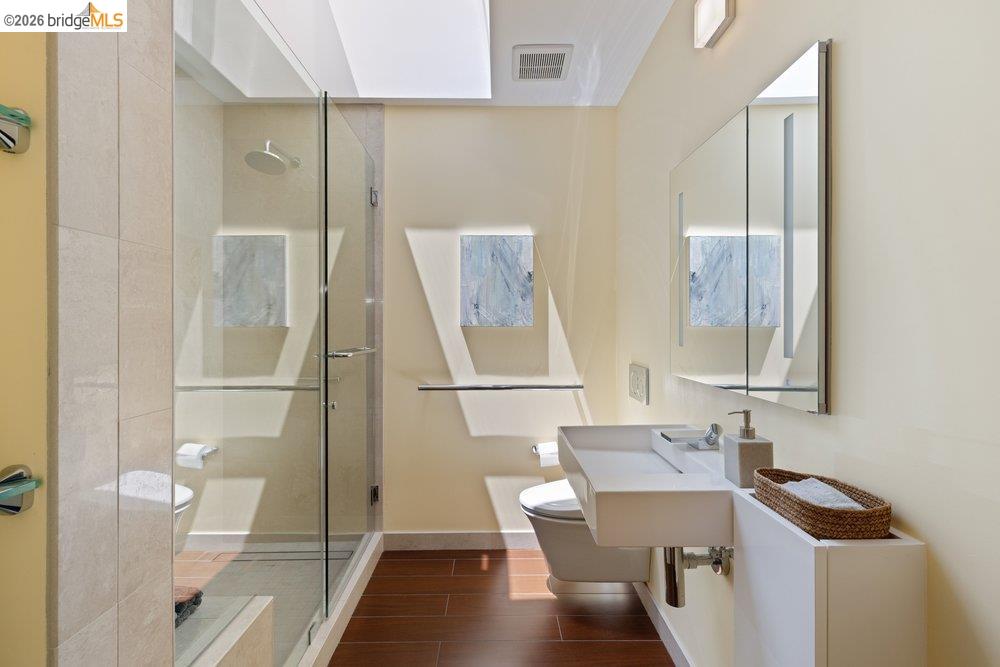 287 Purdue Avenue Kensington, CA 94708 - Photo 47 of 60 Contemporary bathroom featuring a floating vanity with an integrated sink, a frameless glass shower enclosure, wood-finish flooring, and a skylight