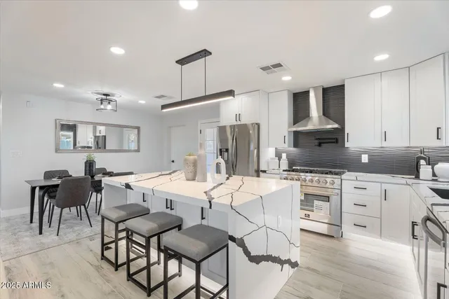 a large kitchen with stainless steel appliances kitchen island granite countertop a dining table chairs refrigerator and sink