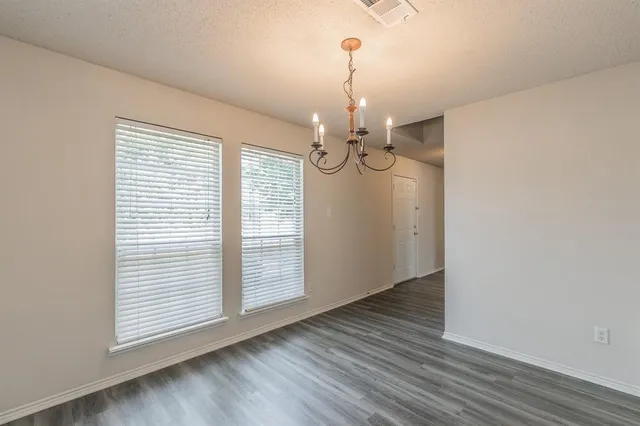 an empty room with wooden floor chandelier and windows