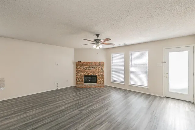 an empty room with wooden floor chandelier fan and windows