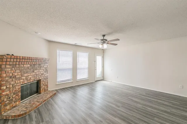 an empty room with wooden floor fireplace and windows