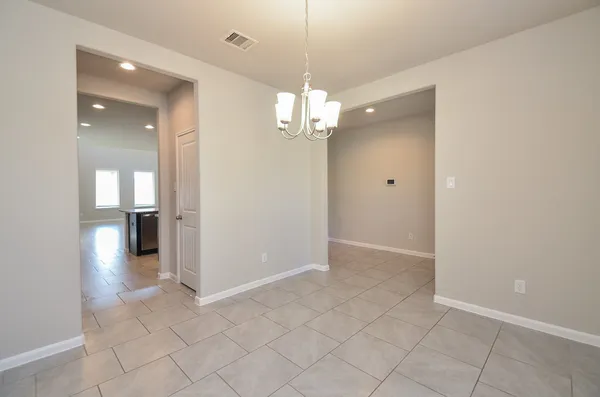 an empty room and kitchen view with a chandelier fan