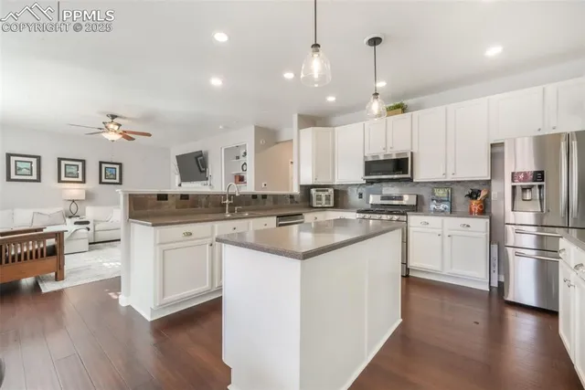 a kitchen with stainless steel appliances kitchen island granite countertop a stove a sink a refrigerator and white cabinets with wooden floor