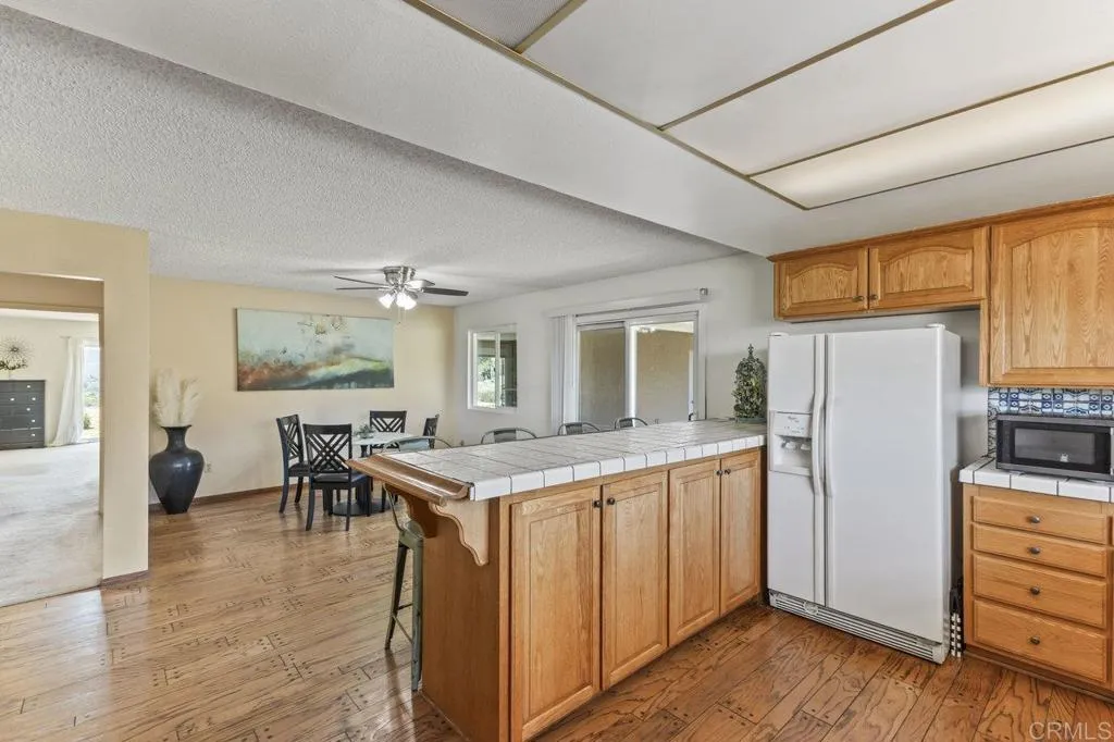 6825 Kellyn Lane Vista, CA 92084 - Photo 21 of 65 a kitchen with granite countertop a refrigerator a stove a dining table and chairs with wooden floor