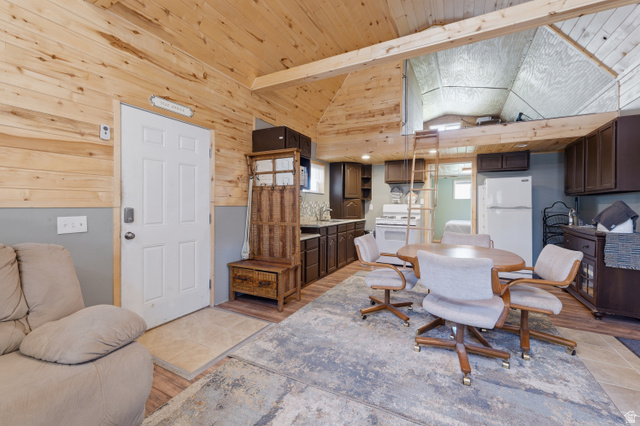 Wood-paneled ceilings with exposed beams, lofted area with ladder access, full kitchen with white appliances, wood-finish flooring, and built-in cabinetry