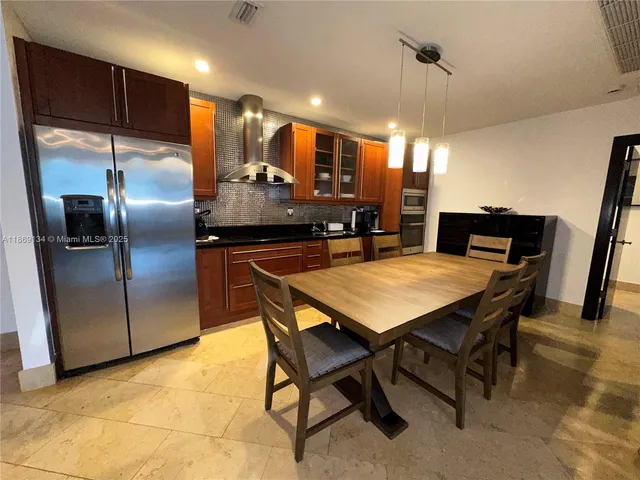 a kitchen with stainless steel appliances kitchen island granite countertop a table chairs and a refrigerator